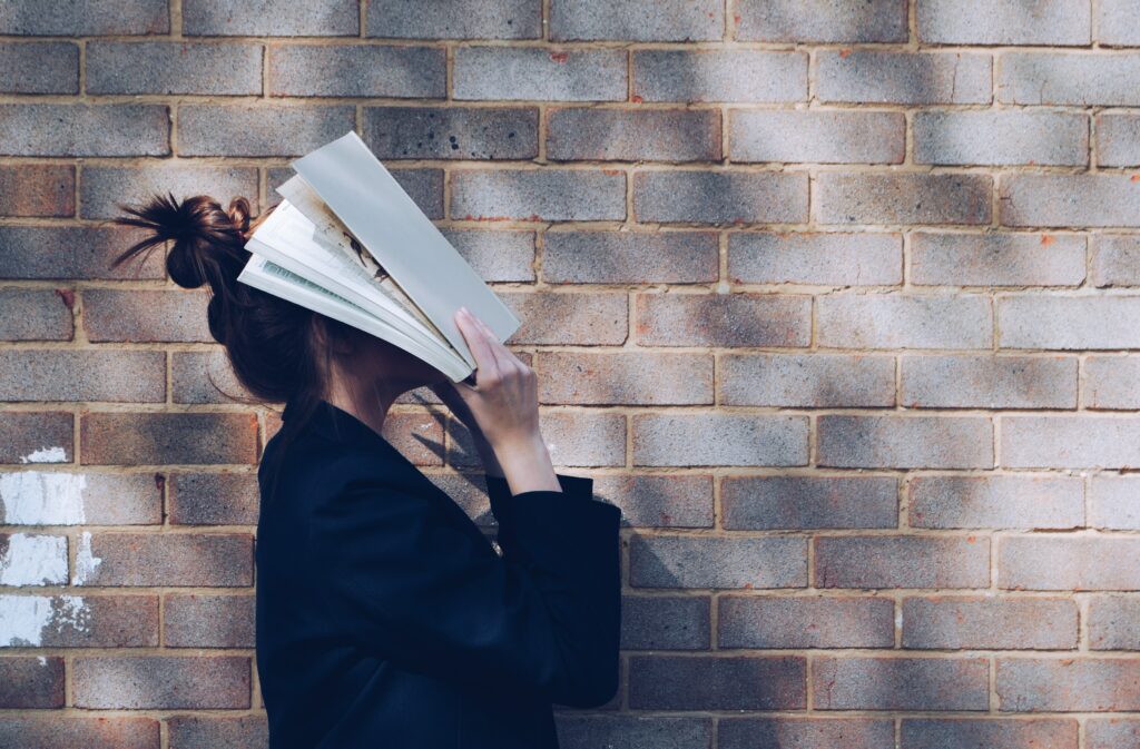 Eine junge Frau, die ihr Gesicht mit einem weißen Buch bedeckt. | Siora Photography on Unsplash